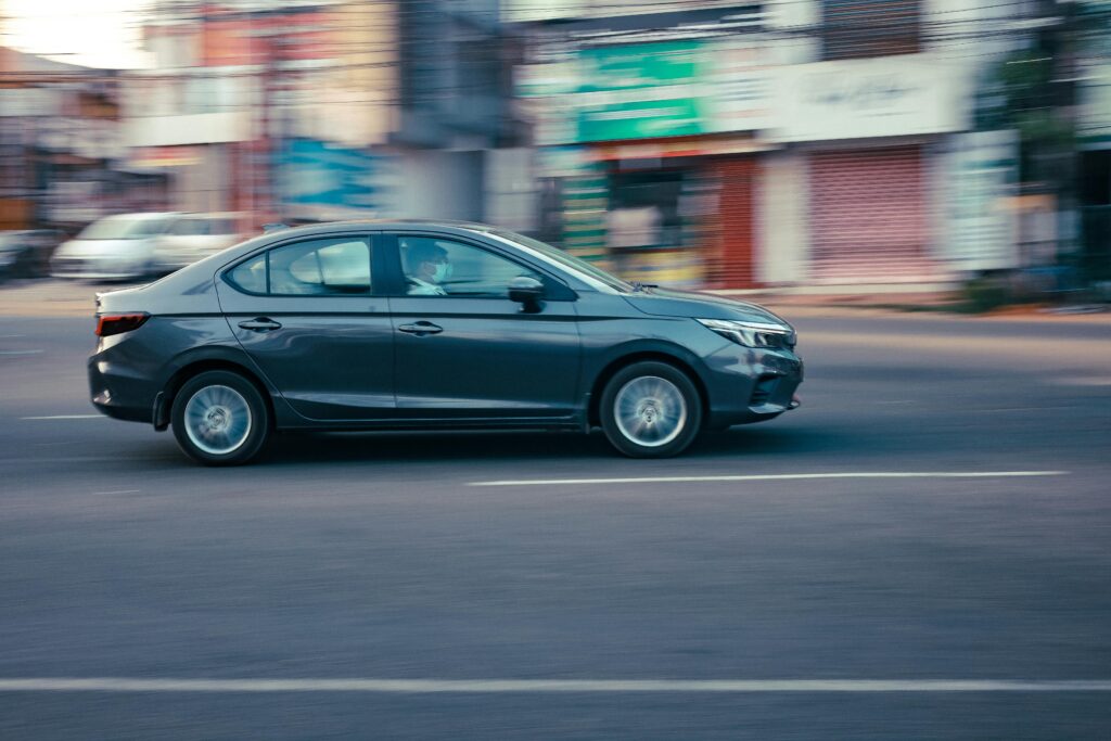 A sleek black sedan speeds through the bustling streets of KL, India, showcasing urban transportation.